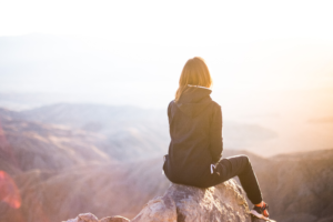 Girl sitting on top of a mountain with her back to the camera