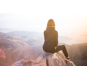 Girl sitting on top of a mountain with her back to the camera