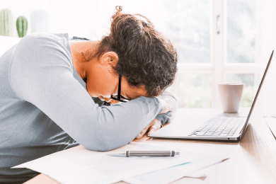 Woman with her head on her desk trying to avoid focusing on the negative comment