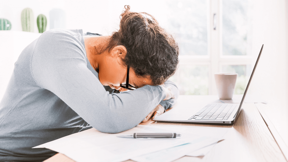 Woman with her head on her desk trying to avoid focusing on the negative comment