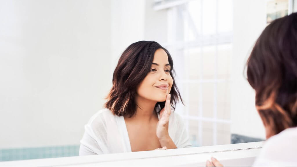 Woman looking in the mirror, talking postively to herself as an act of loving yourself more