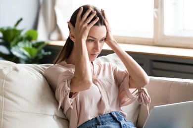 A woman with her hands holding her head looking at her laptop is experiencing confidence killers.
